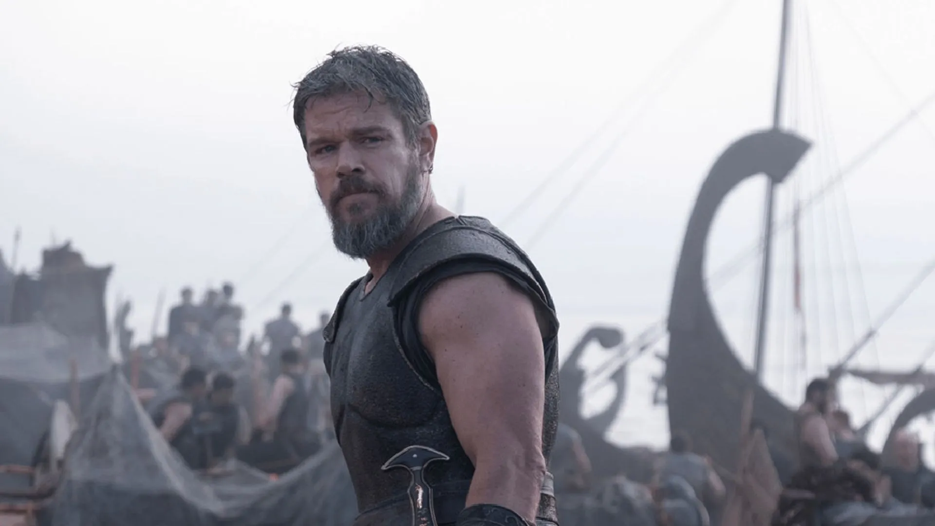 Matt Damon como Odisseu com barba e armadura desgastada, olhando para o mar em cena de A Odisseia de Christopher Nolan