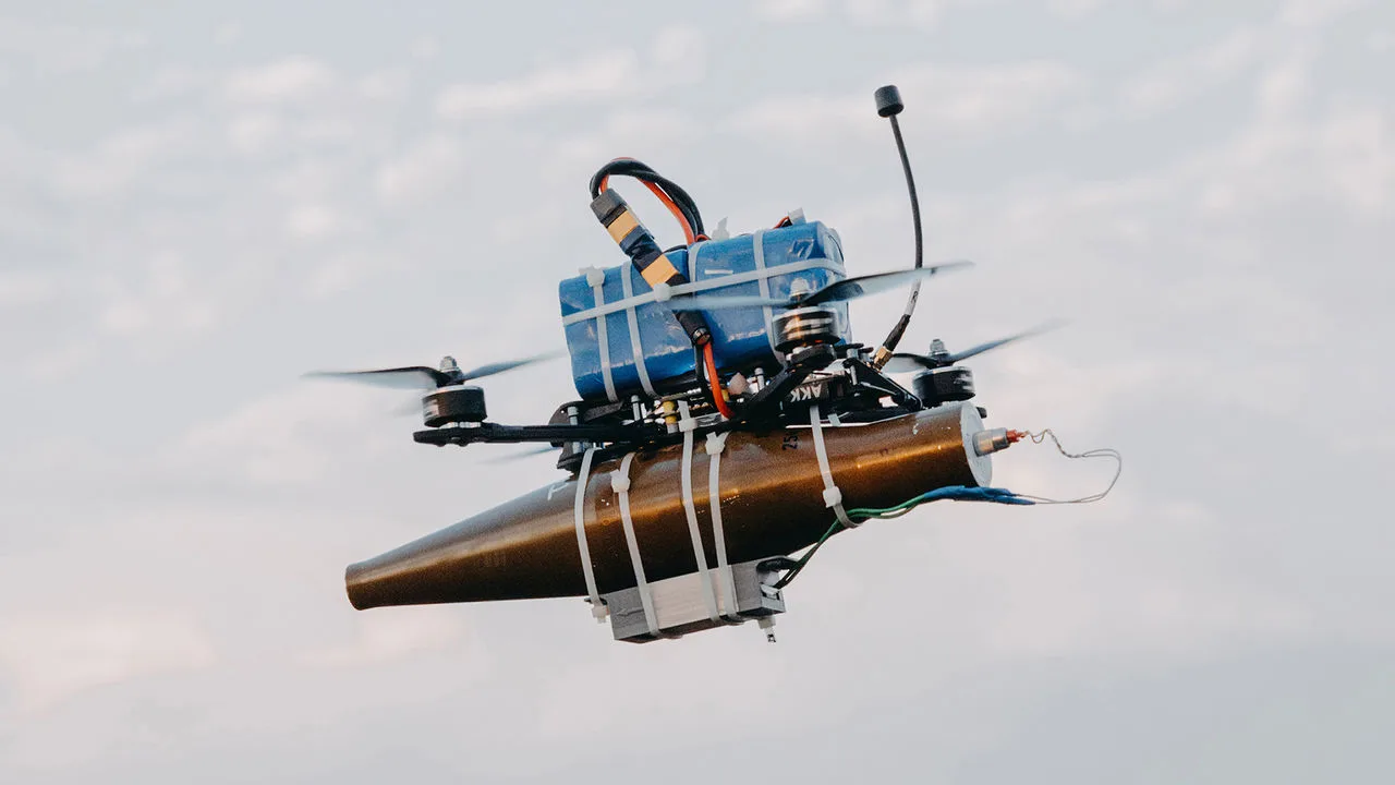 Drone leve em voo com uma ogiva de RPG presa à estrutura por abraçadeiras plásticas, bateria de lítio fixada com fita em cima e antena na traseira