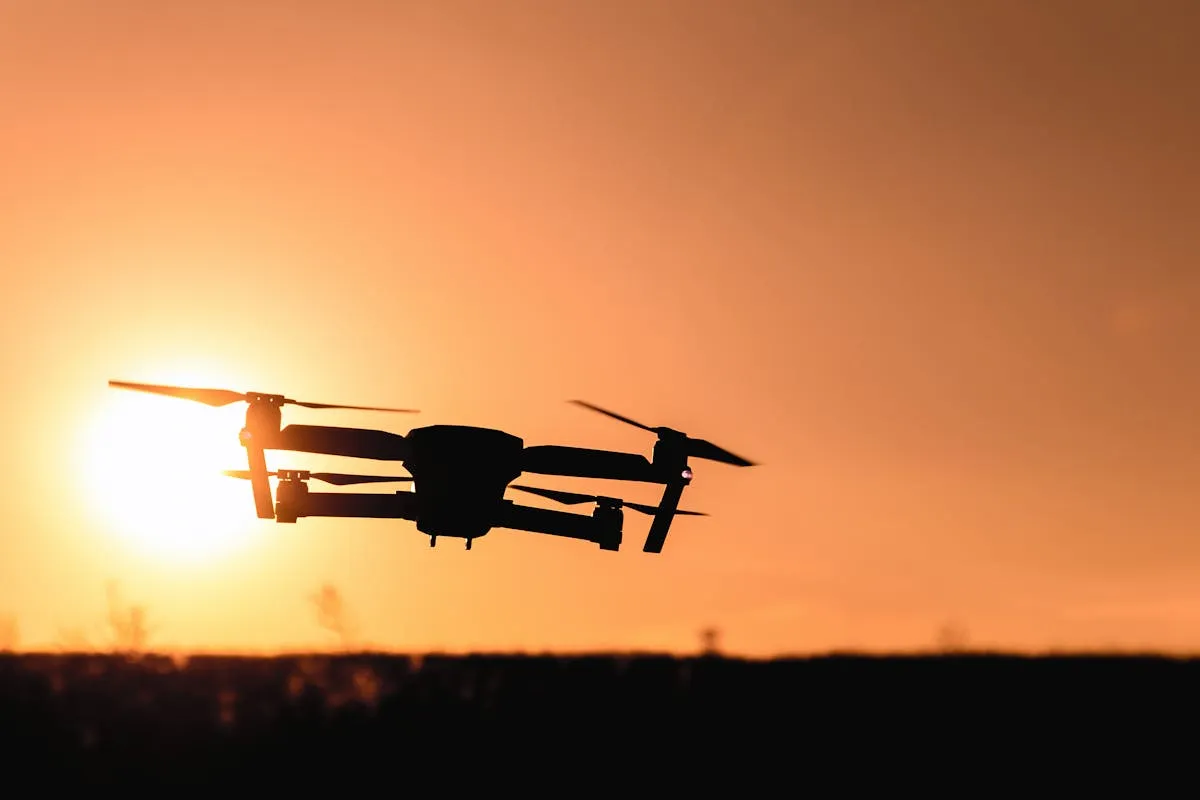 Silhueta de drone voando contra o pôr do sol alaranjado evocando armas autônomas e tecnologia militar