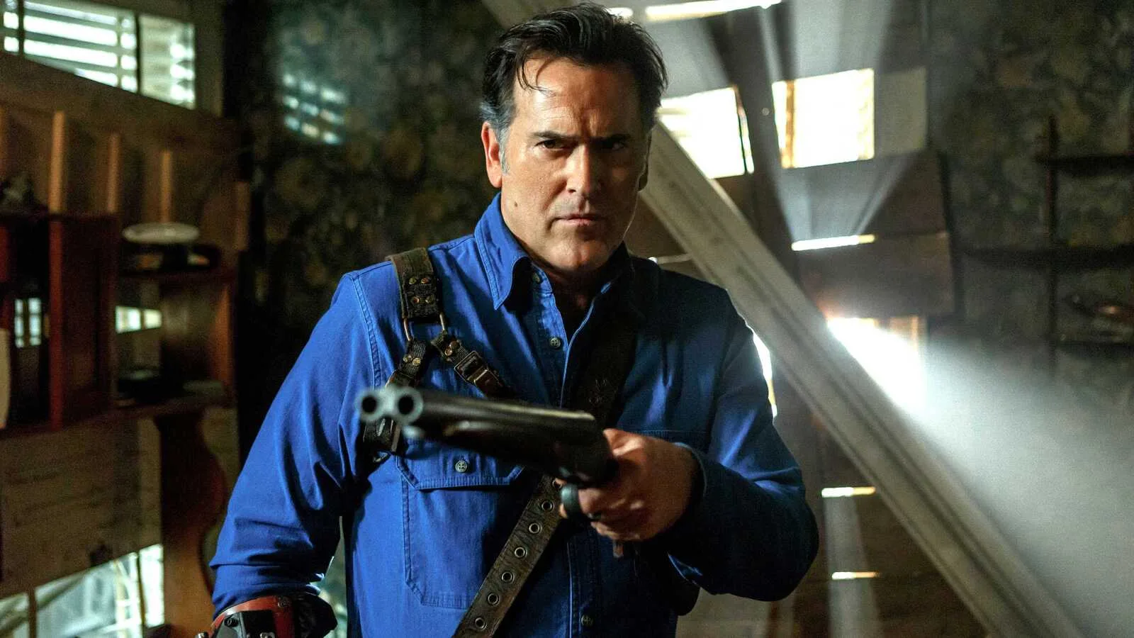 Bruce Campbell como Ash apontando a espingarda dentro da cabana, em cena de Ash vs Evil Dead