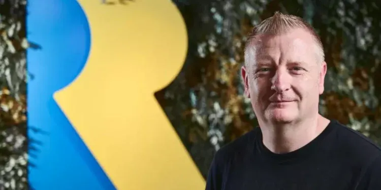 Craig Duncan, chefe do Xbox Game Studios, posando diante do logotipo da Rare; ele pediu demissão no mesmo dia em que vazou o plano de fechamento de estúdios