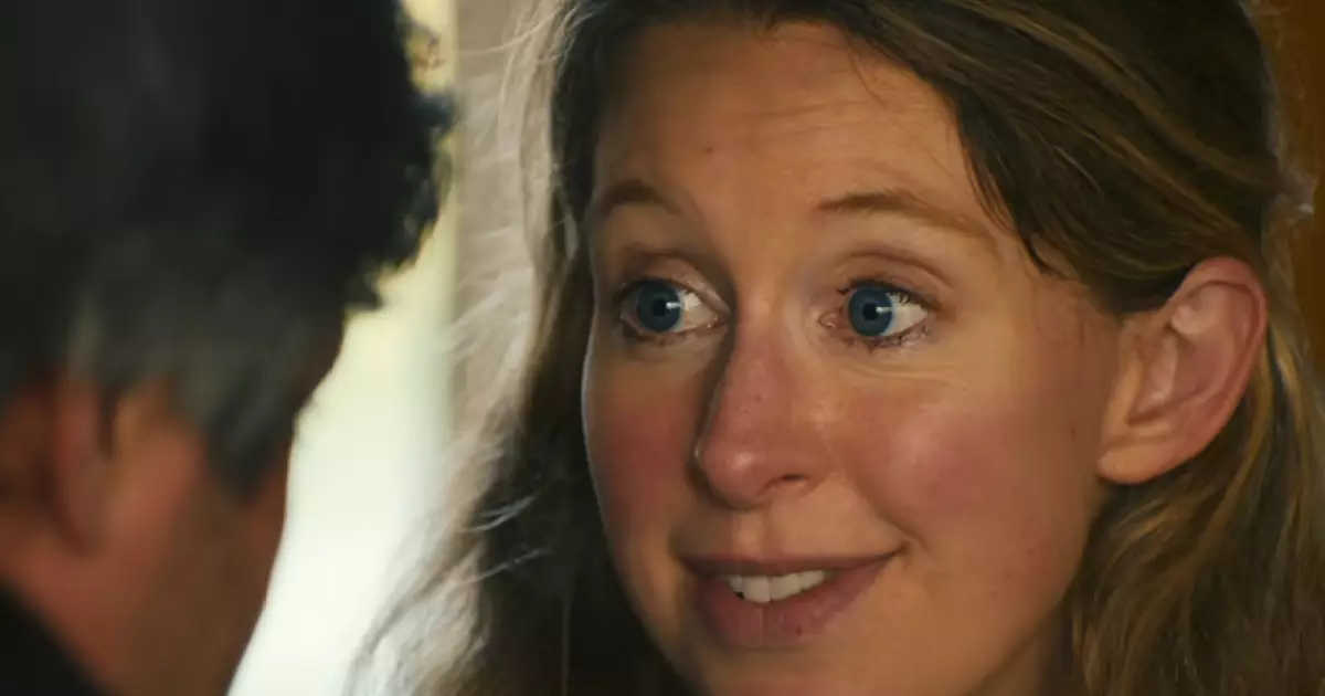 Close no rosto de Elizabeth Holmes, olhos arregalados, falando com alguém que aparece de costas e fora de foco em primeiro plano