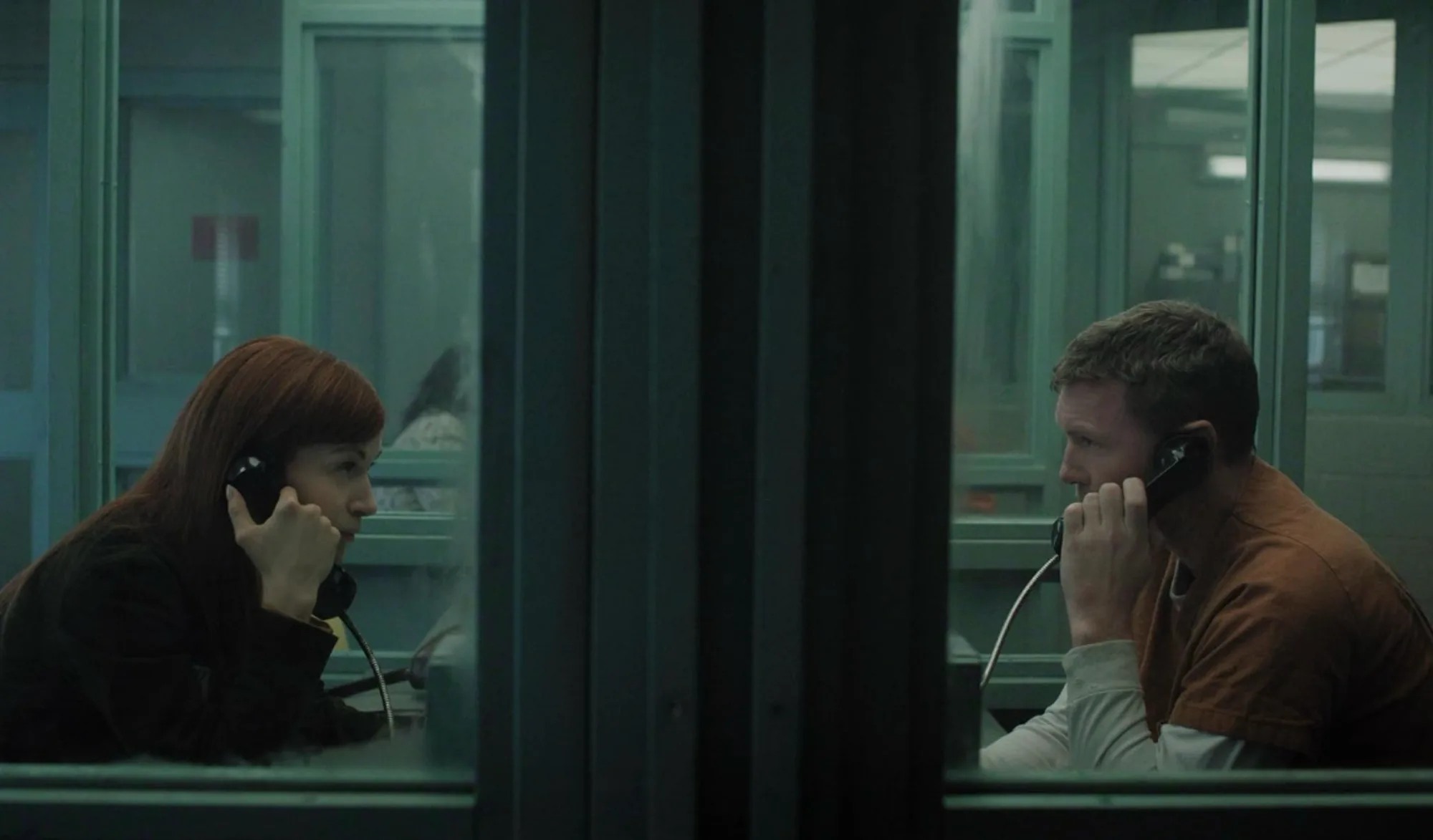 Britt Lower e Sam Worthington conversando por telefone separados pelo vidro da sala de visitas de uma prisão, em cena de I Will Find You