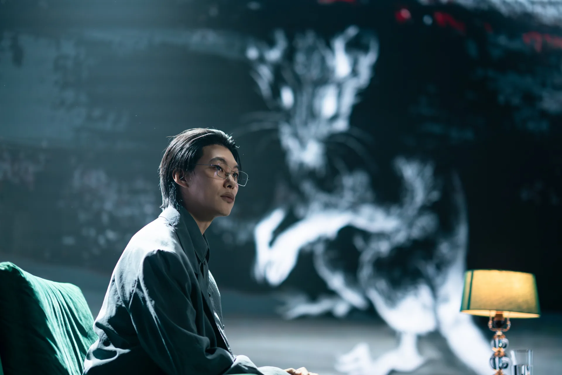 Je Moon-jae, vivido por Ryu Jun-yeol, sentado de óculos num sofá verde e olhando para cima, com a silhueta ampliada de um rato projetada na parede atrás dele