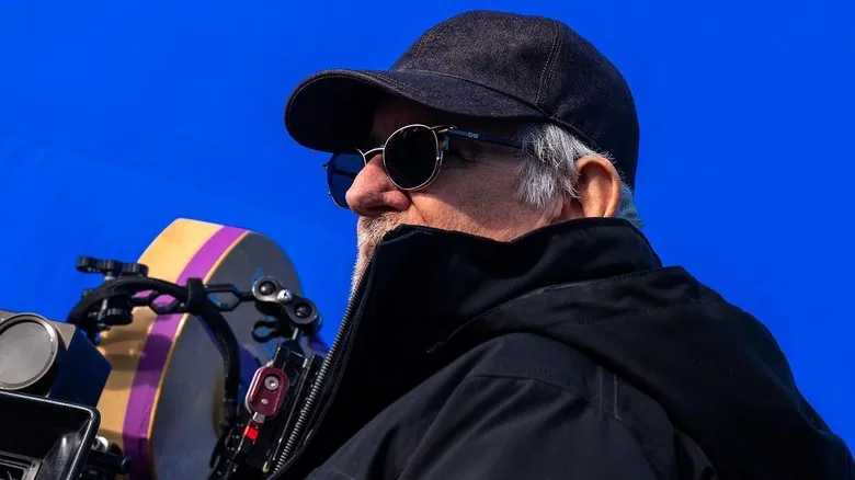 Steven Spielberg no set de filmagem observando o horizonte aberto, com câmera ao lado e luz de pôr do sol ao fundo