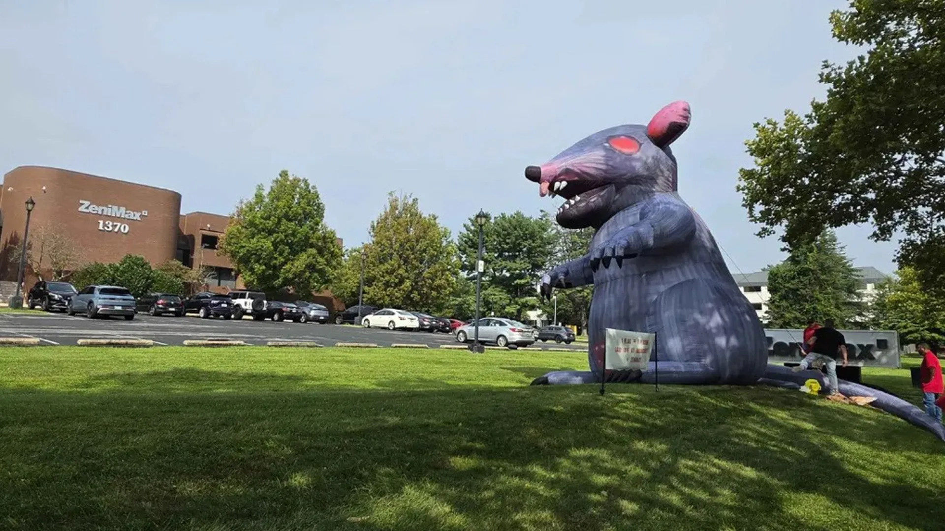 Rato inflável gigante cinza, de olhos vermelhos e dentes à mostra, montado no gramado em frente ao prédio da ZeniMax em Rockville durante protesto sindical contra as demissões do Xbox